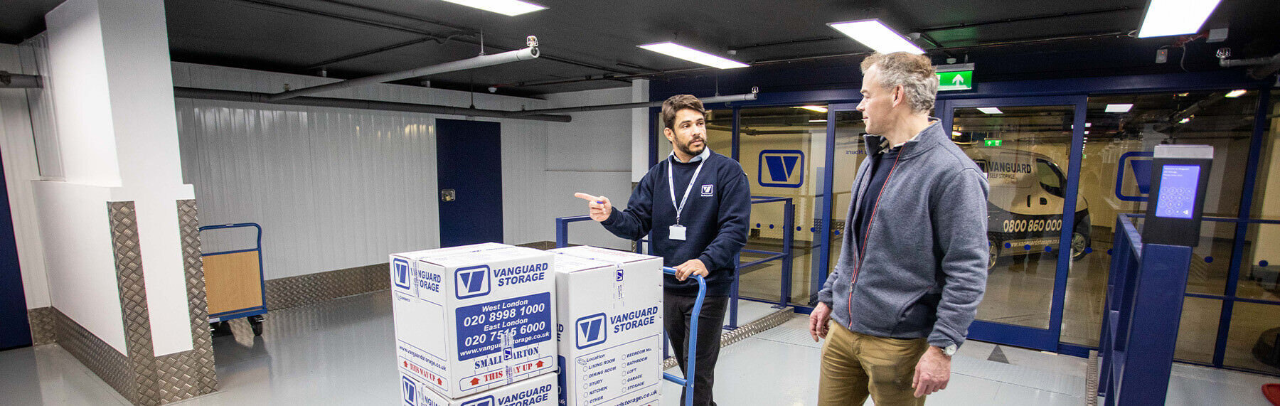 A photo showing a Vanguard employee helping a customer take Vanguard boxes into a storage unit.